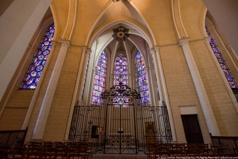 Side chapel in Chartres Cathedral with wrought-iron gate, altar, tall stained-glass lancets, and pointed vaults.