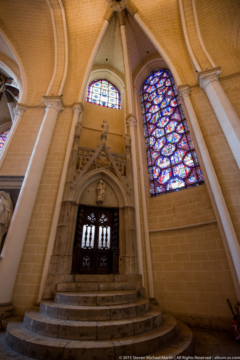 Stone doorway reached by steps beneath stained-glass windows and pointed vaulting inside Chartres Cathedral.