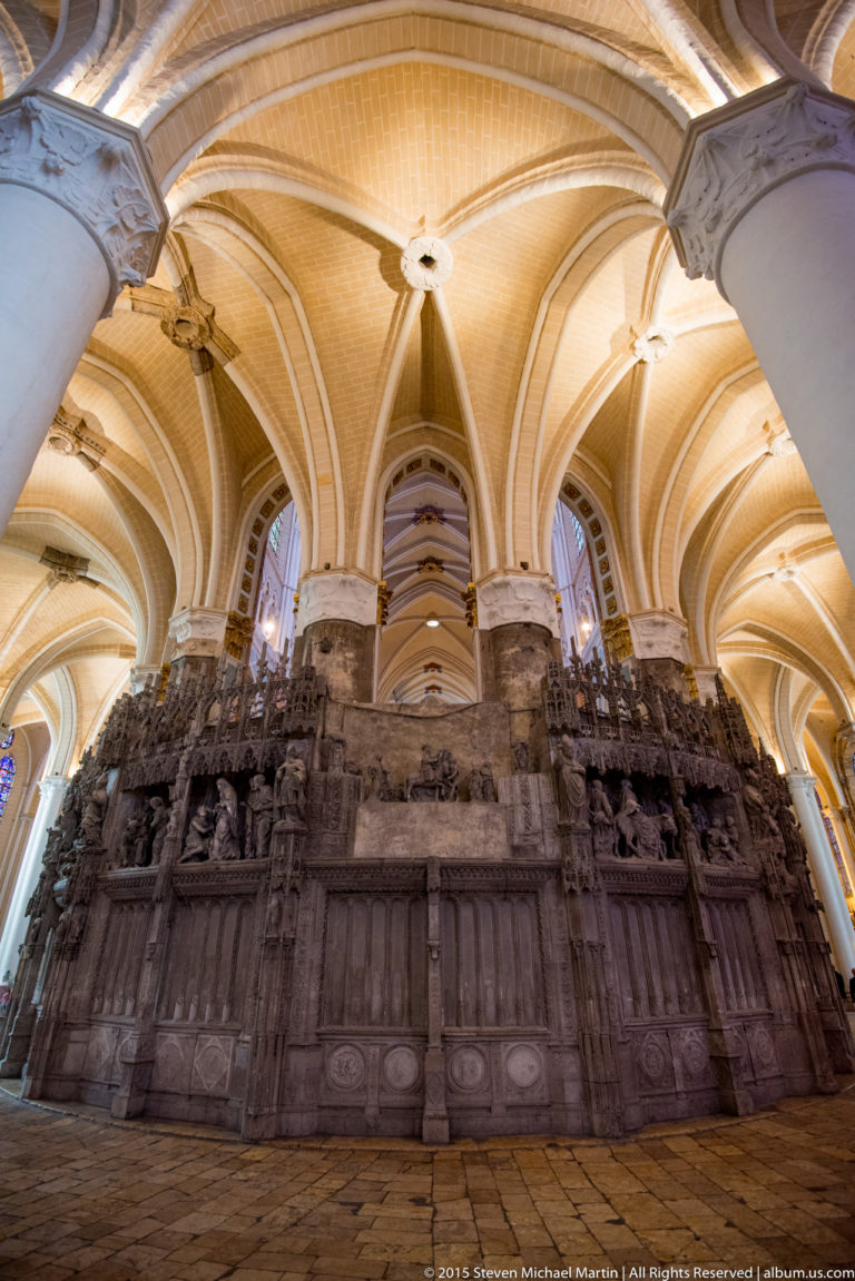 Wide low-angle view of the carved choir screen extending beneath massive piers and ribbed vaults in Chartres Cathedral.