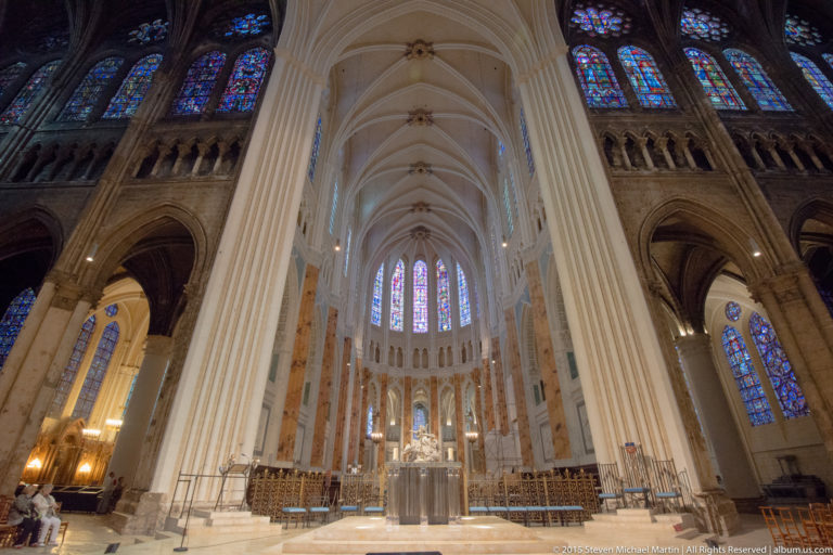 Central view toward the altar and soaring apse of Chartres Cathedral, framed by tall pale piers and stained glass.