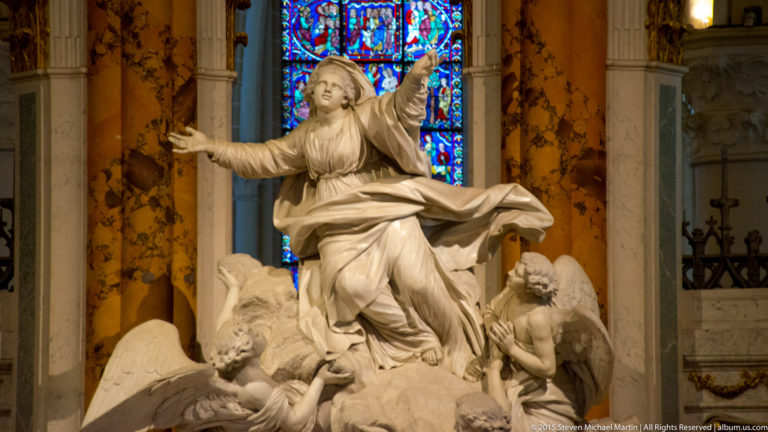 Close view of the Virgin Mary with outstretched arms above winged angels, backed by stained glass in Chartres Cathedral.