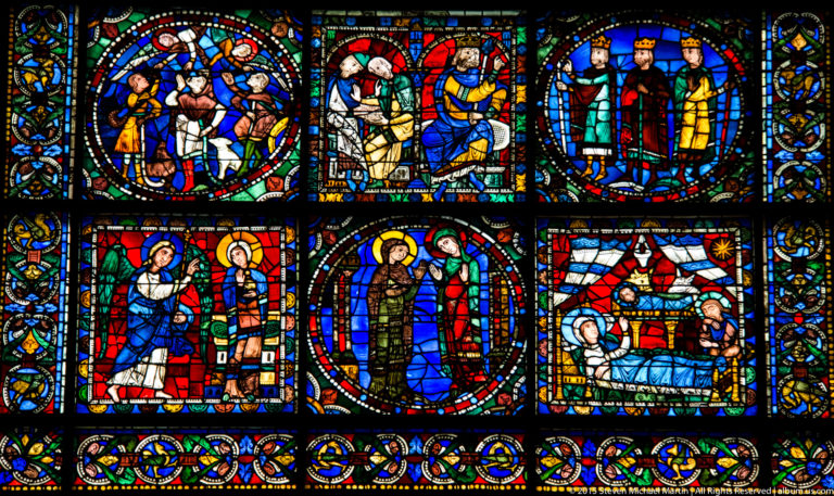 Close view of colorful medieval stained-glass panels with haloed figures, narrative scenes, and ornamental borders at Chartres Cathedral.