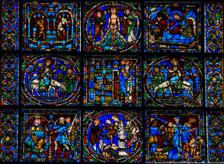 Stained-glass window composed of rows of circular narrative medallions with figures in blue, red, and green glass.