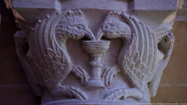 Close view of a weathered carved stone capital with stylized faces and foliage at Chartres Cathedral.