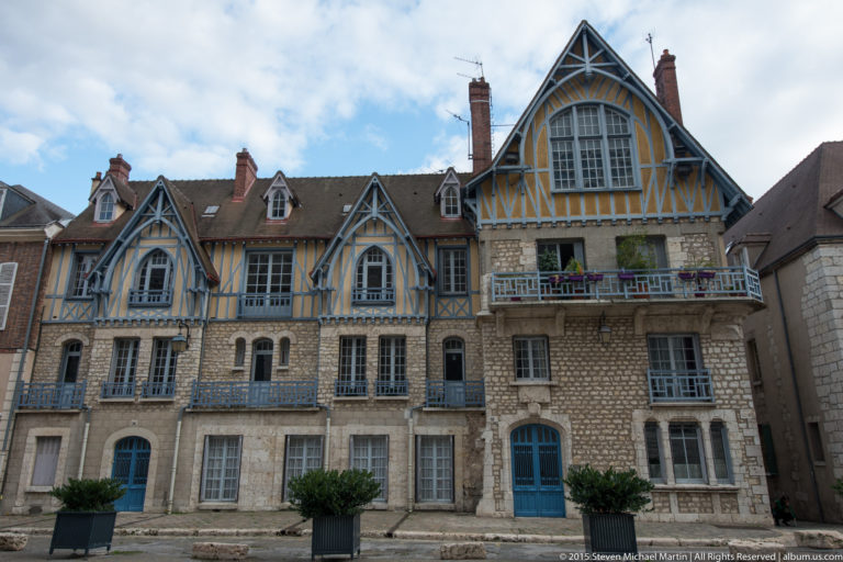 Large historic building with stone lower stories and blue-and-ochre timber-framed gables, balconies, and tall windows in Chartres.