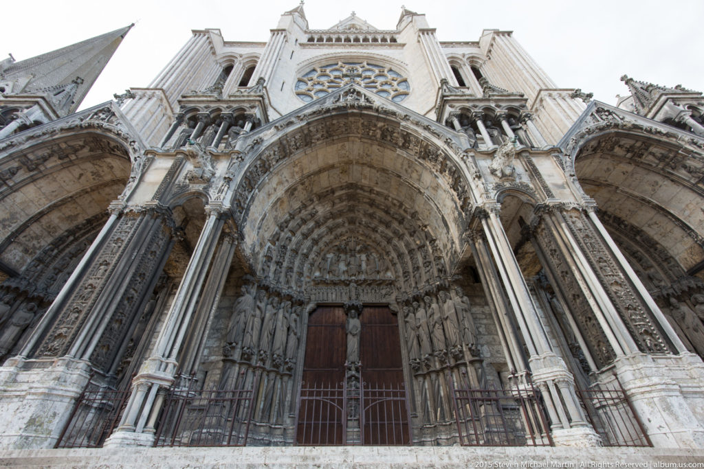 Close low-angle view of the central north-transept portal at Chartres Cathedral with deep archivolts, jamb statues, and wooden doors.