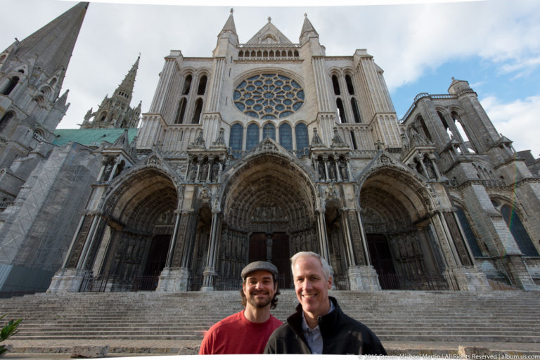 Two men posing in front of the broad steps and sculpted north-transept façade of Chartres Cathedral.