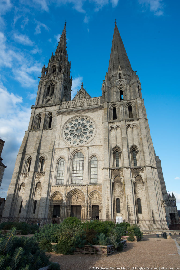 Frontal view of Chartres Cathedral’s west façade with unequal spires, central rose window, tall lancets, and lower portals.