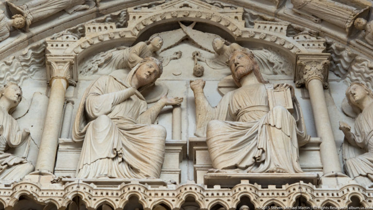 Two seated robed figures facing each other within an ornate carved stone niche on a portal of Chartres Cathedral.