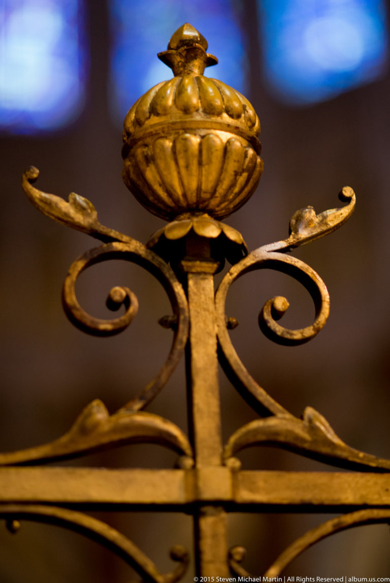 Close-up of a gilded floral finial and symmetrical scrolling ironwork inside Chartres Cathedral.