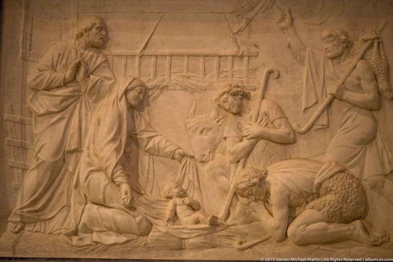 Shallow relief with several robed figures gathered around a central seated or reclining figure inside Chartres Cathedral.