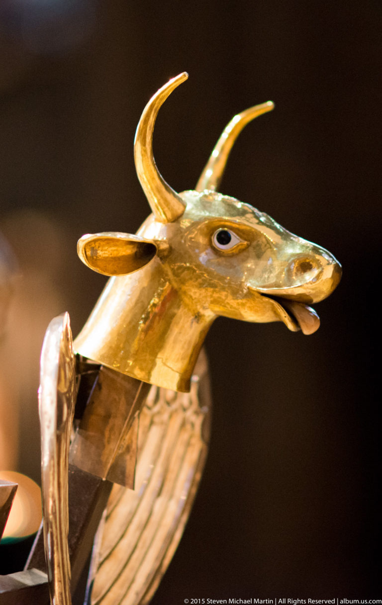 Close-up of a gilded horned animal head with long muzzle, pointed ears, curved horns, and decorative metal surfaces.