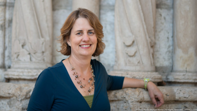 Smiling woman in a blue top leaning against carved stonework outside Chartres Cathedral.