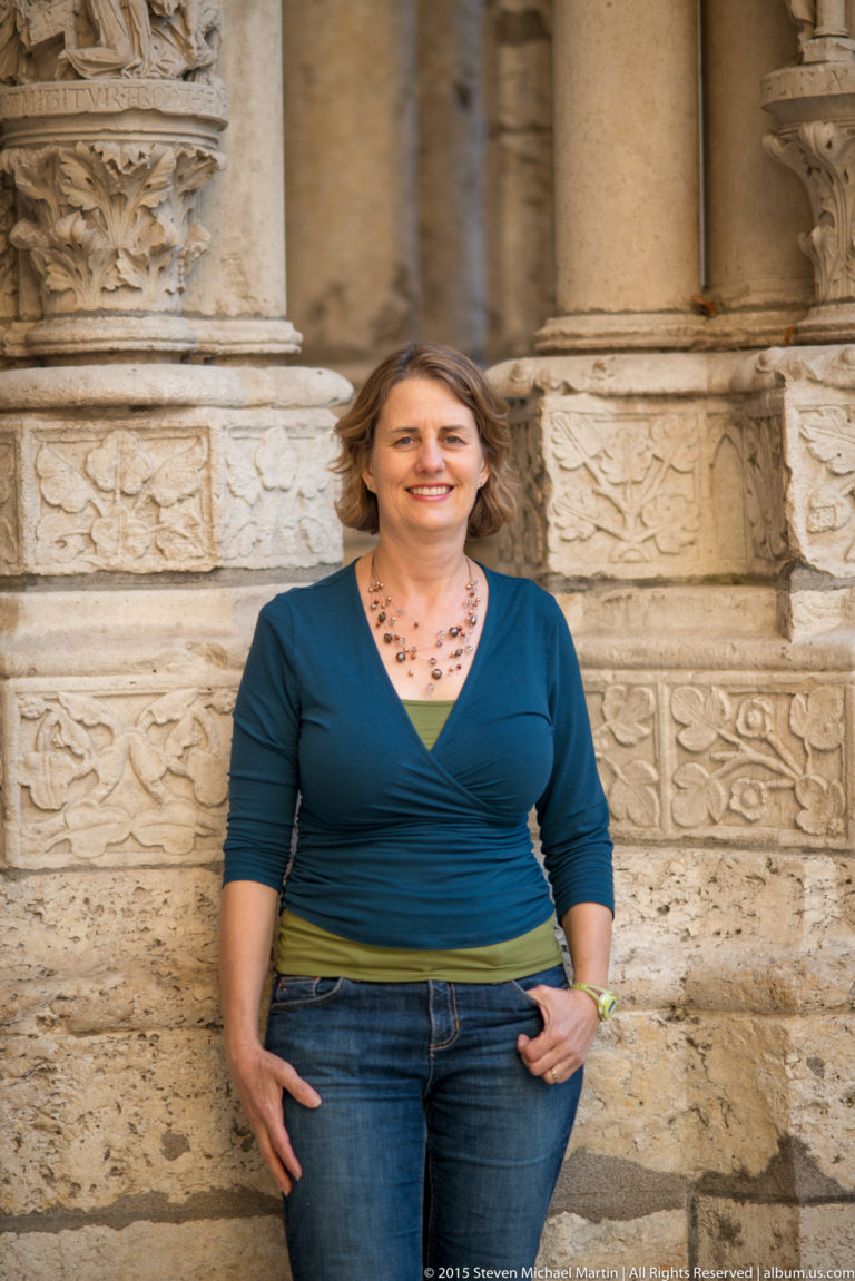 Woman in a blue top and jeans standing against rows of carved stone blocks at Chartres Cathedral.
