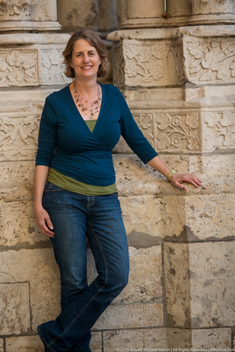 Full-body portrait of a woman leaning against carved stone blocks on the exterior of Chartres Cathedral.
