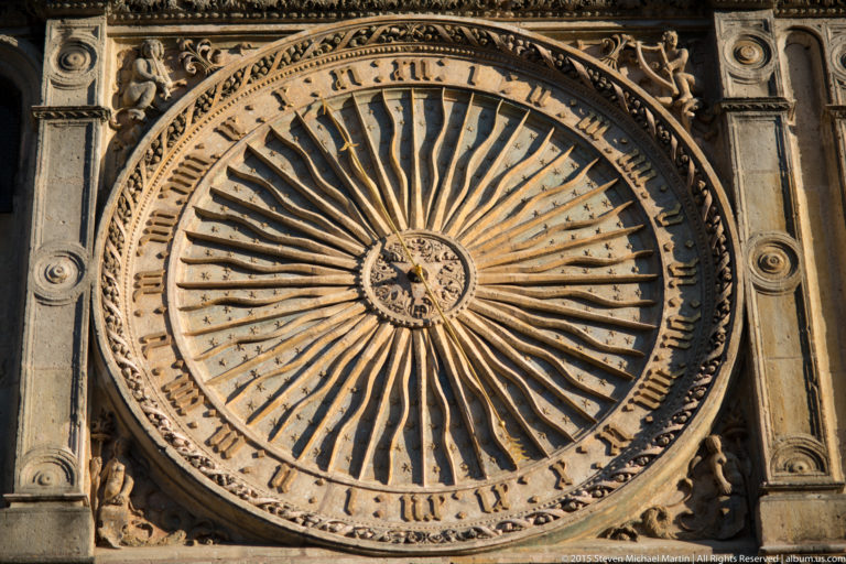 Close view of Chartres Cathedral’s circular historic clock with numbered ring, radiating bars, central dial, and ornate frame.
