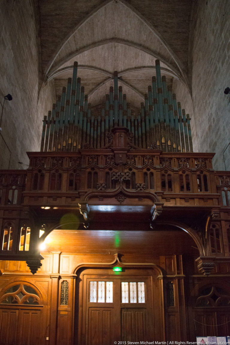 Pipe organ with tall metal pipes in an ornate dark wooden case, viewed from below inside Église Saint-Malo.