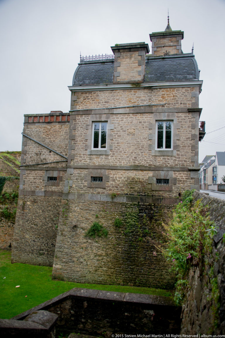 Stone building with slate roof above thick masonry walls and a defensive ditch in Dinan’s historic fortified center.