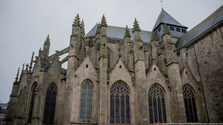 Upward exterior view of Église Saint-Malo with tall traceried windows, buttresses, pinnacles, and slate roofs.