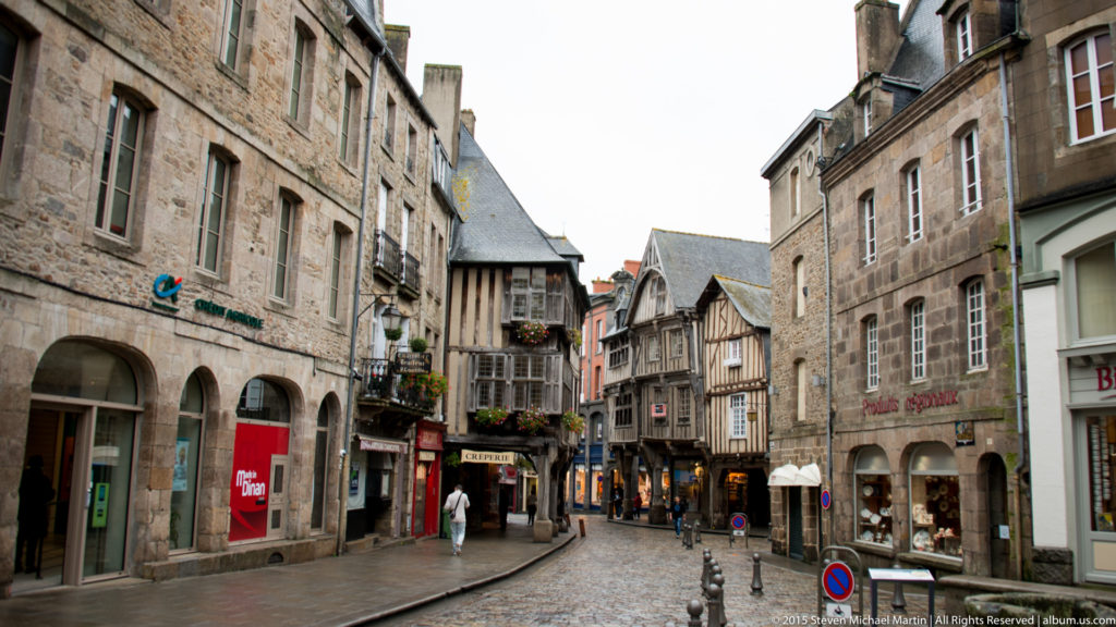 Curving Dinan street lined with stone buildings, timber-framed upper stories, shops, and slate roofs.