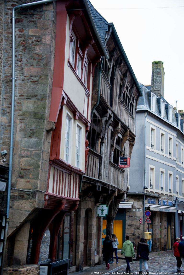 Red and dark timber-framed historic houses with projecting upper floors above pedestrians and shops in Dinan.