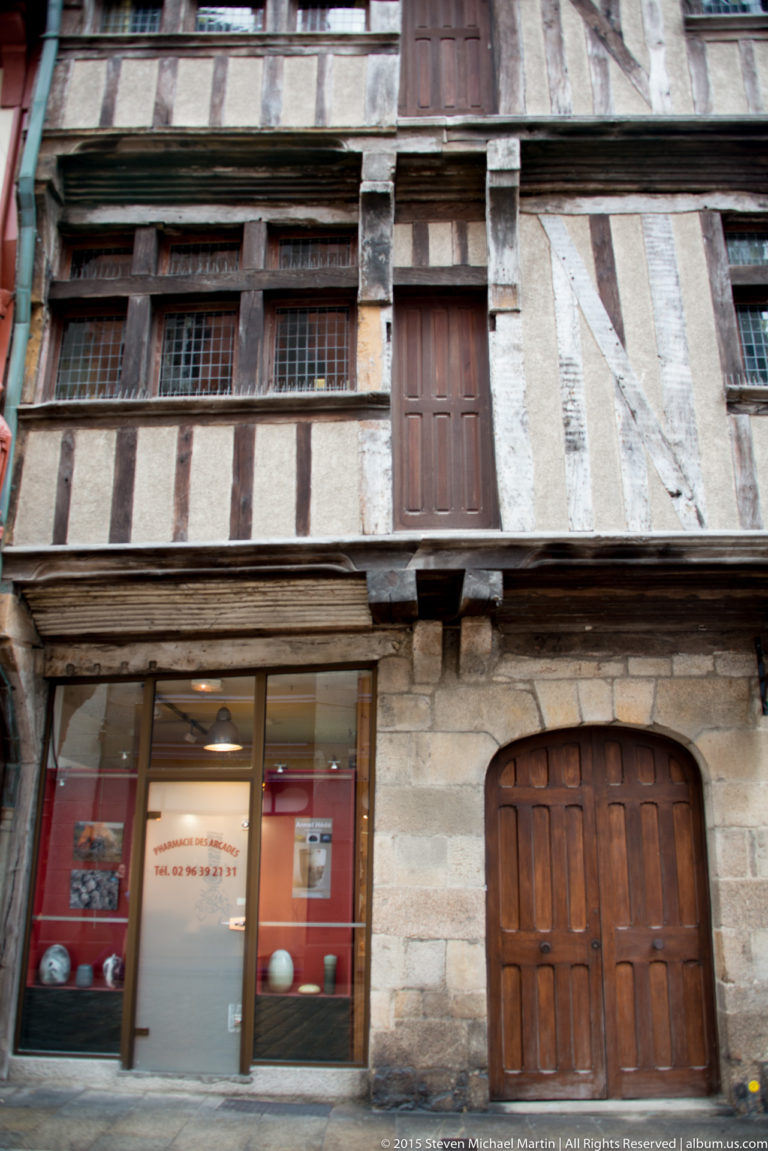 Close view of a historic Dinan half-timbered façade with heavy beams, pale infill, projecting upper floor, and shopfront below.