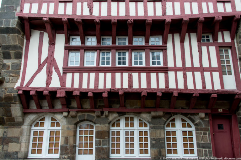 Close view of red-and-white half-timbered upper stories with projecting beams, diagonal braces, and multi-pane windows in Dinan.