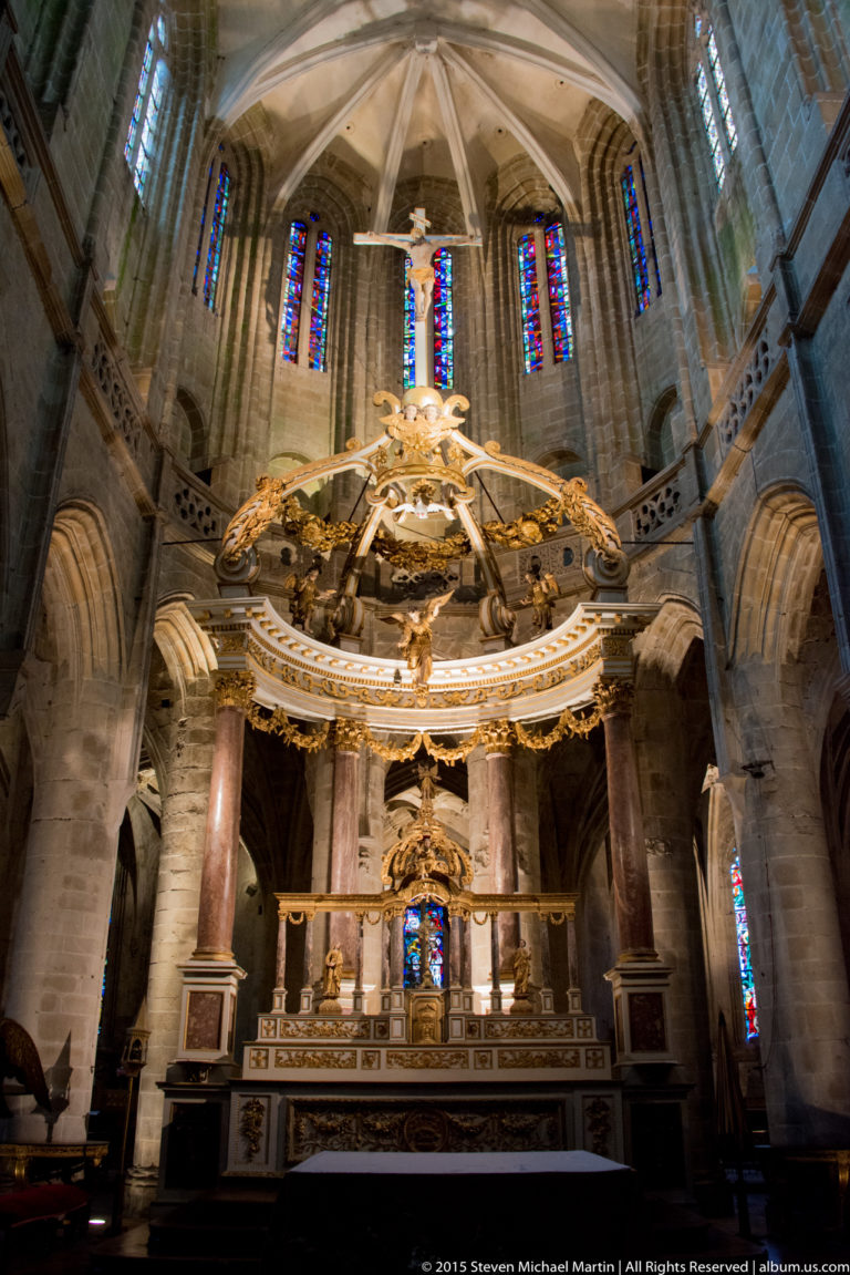 Large gilded altar canopy with columns and sculptural decoration beneath ribbed vaulting and stained glass in the Basilique Saint-Sauveur.