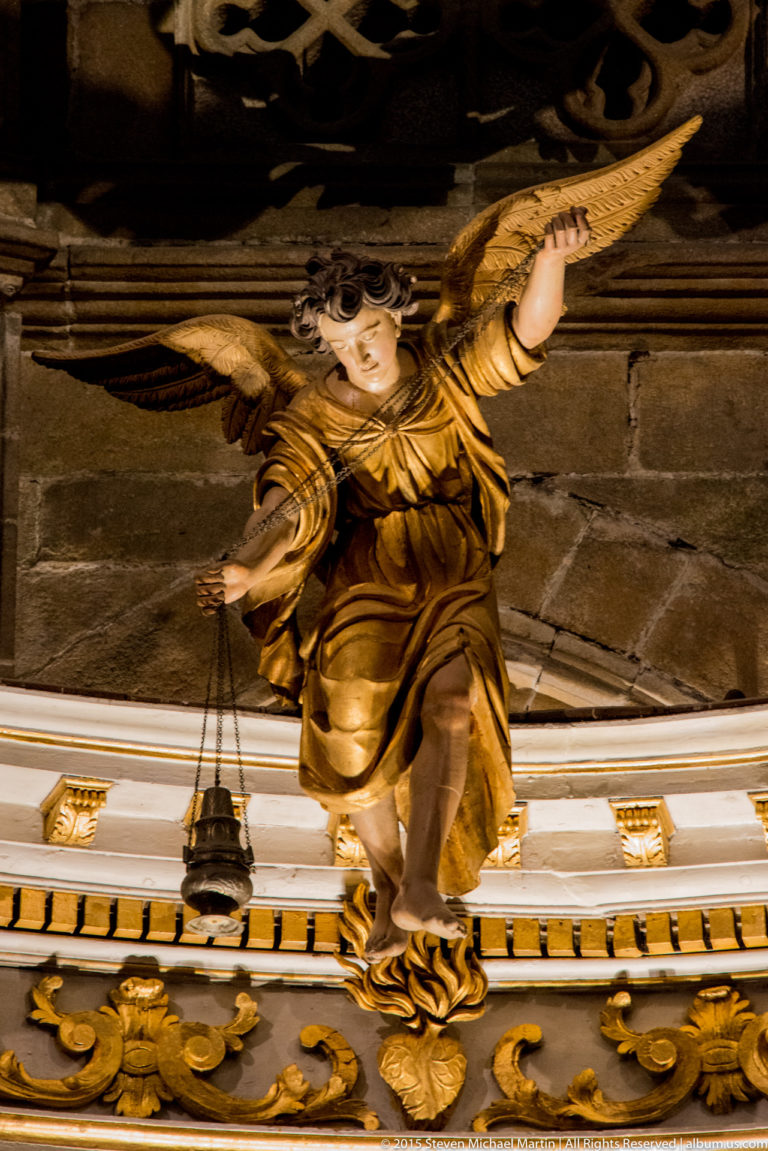 Gilded winged angel sculpture projecting from an ornate church altar canopy against dark stone masonry.