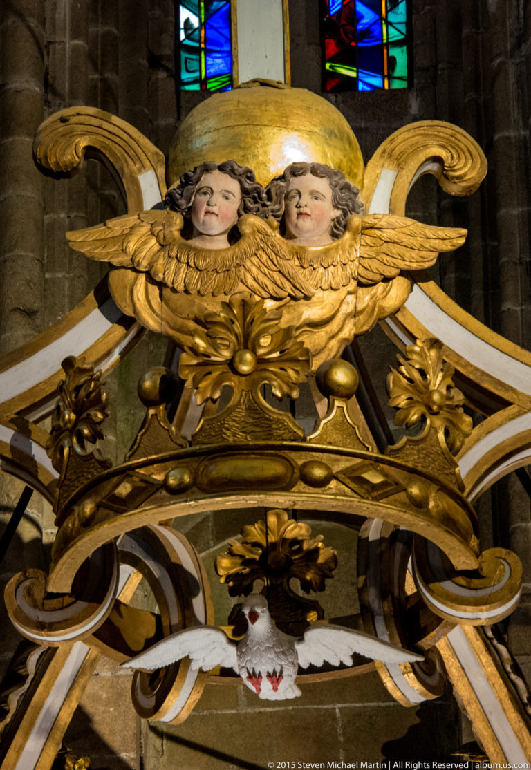 Pair of gilded cherub heads with wings and scrollwork on an ornate altar inside the Basilique Saint-Sauveur.