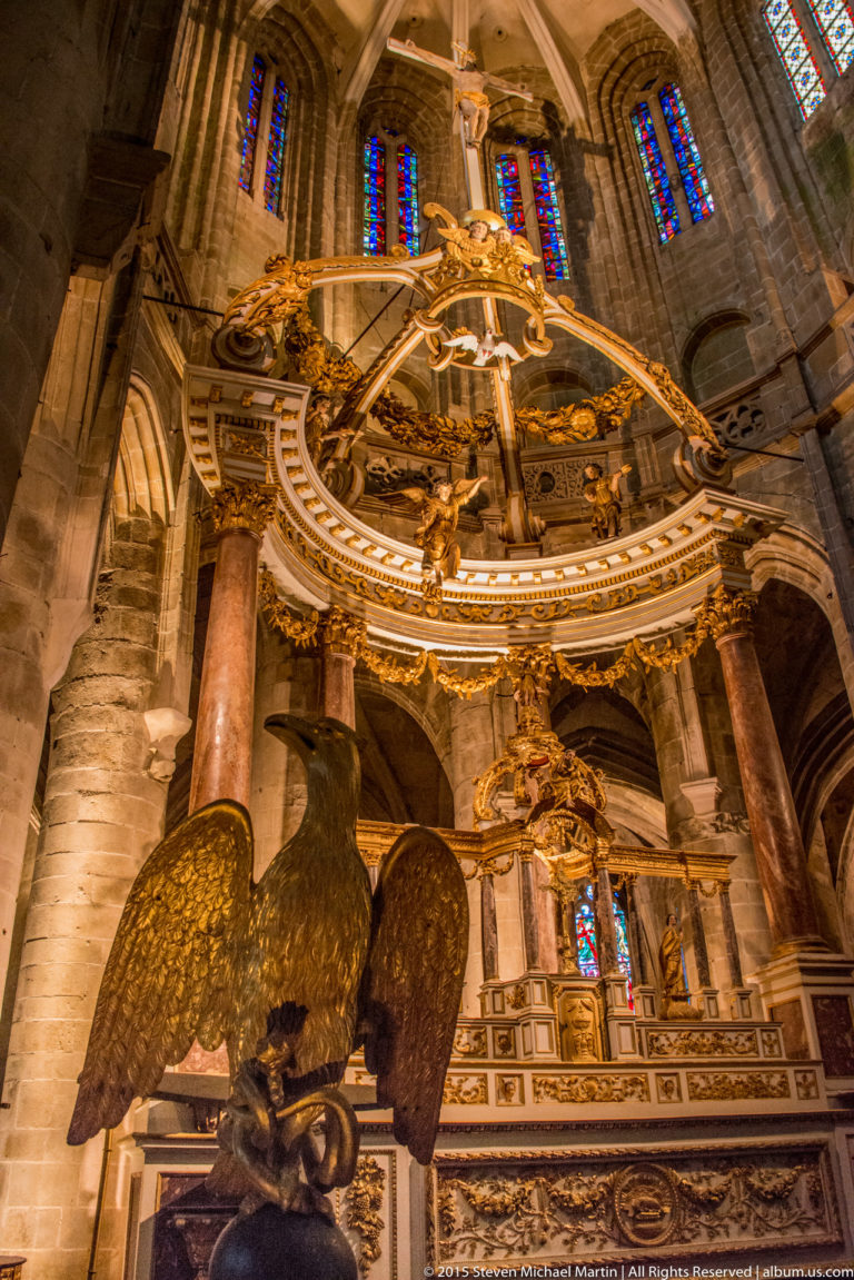 Low-angle view of an ornate gilded altar canopy with a large eagle sculpture beneath ribbed vaults in the Basilique Saint-Sauveur.