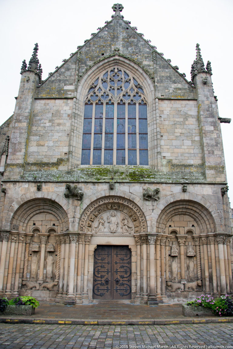 West façade of the Basilique Saint-Sauveur with three Romanesque portal bays and a large Gothic traceried window above.