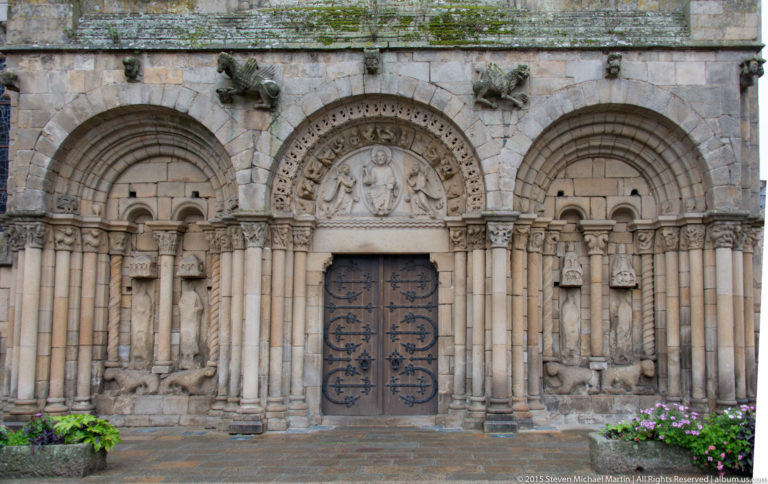 Frontal view of the Basilique Saint-Sauveur portal zone with rounded arches, columns, carved capitals, reliefs, and sculpted figures.