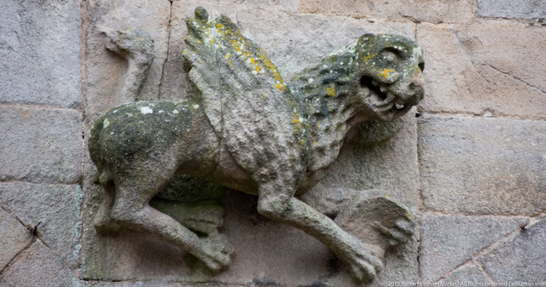 Weathered winged stone grotesque with open mouth and clawed limbs projecting from the wall of the Basilique Saint-Sauveur.