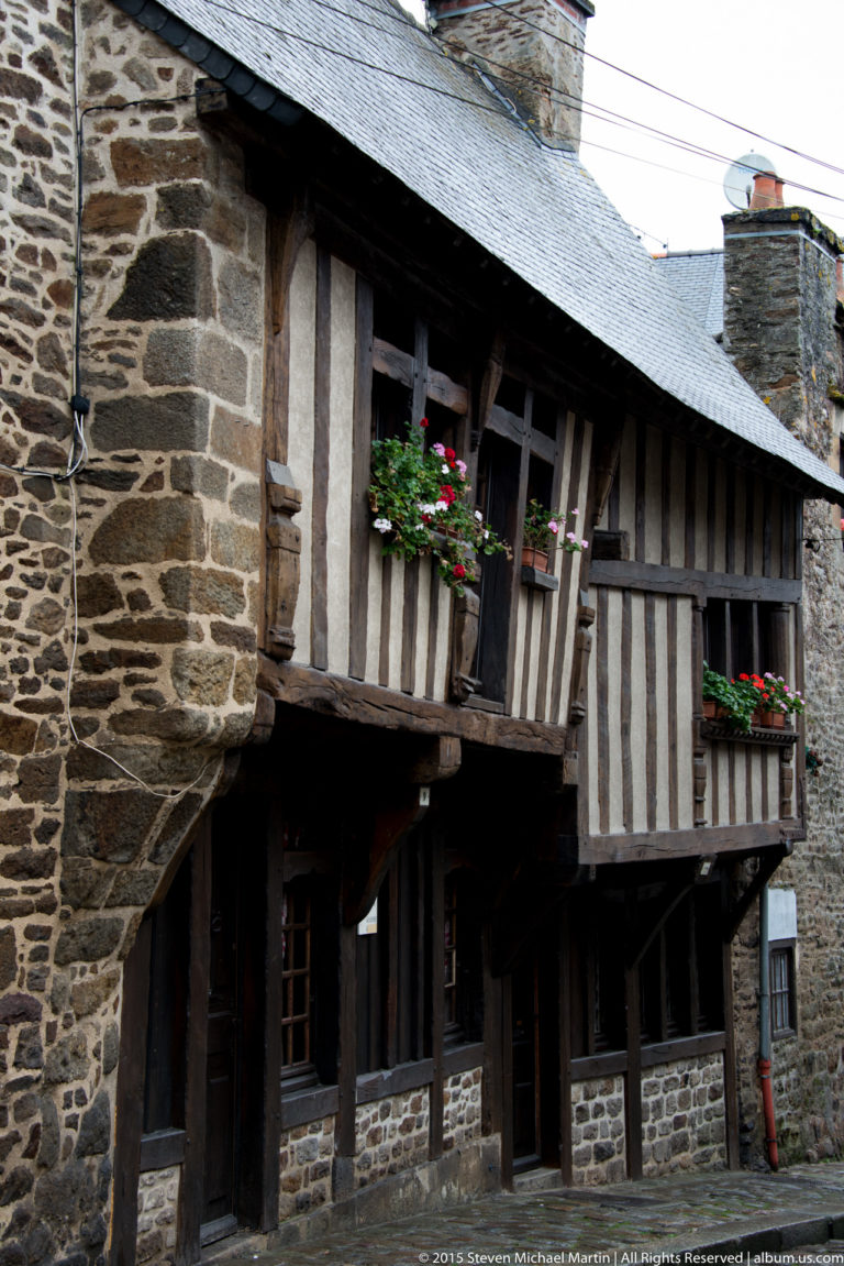 Historic Dinan house with rough stone walls, projecting half-timbered upper floor, slate roof, and flower boxes.