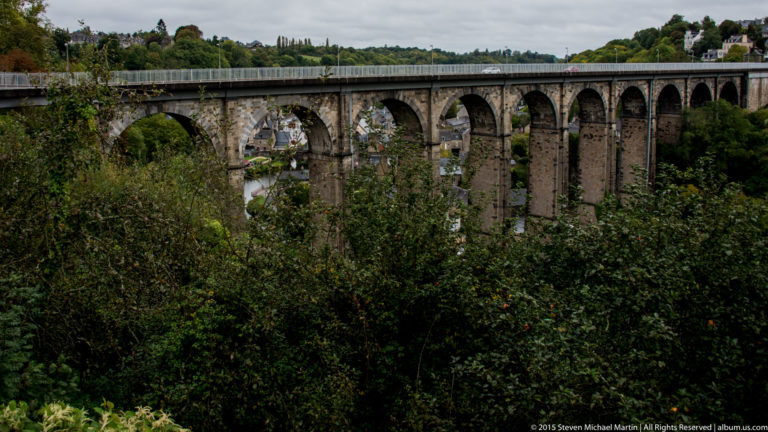 Long stone viaduct with repeated tall arches crossing the wooded Rance valley above lower Dinan.
