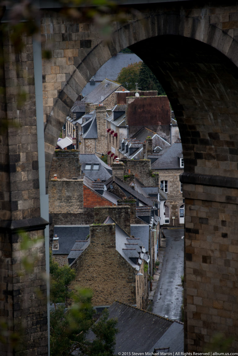 Lower Dinan’s stone houses and slate roofs seen through the dark opening of a massive stone viaduct arch.
