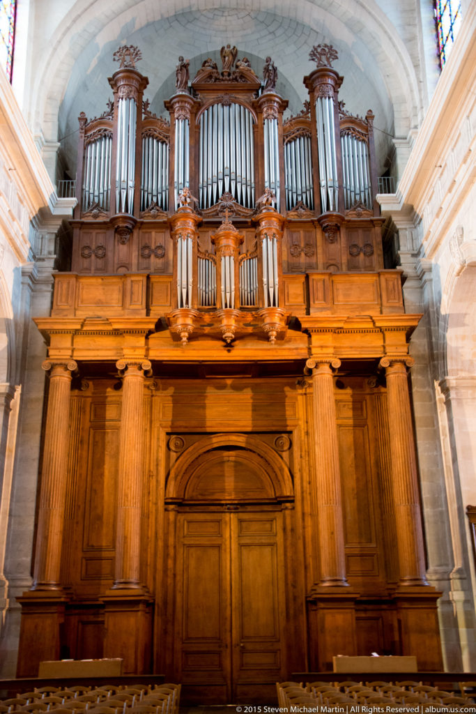 Large church pipe organ with ranks of metal pipes set in an elaborate carved wooden case beneath the stone vault.