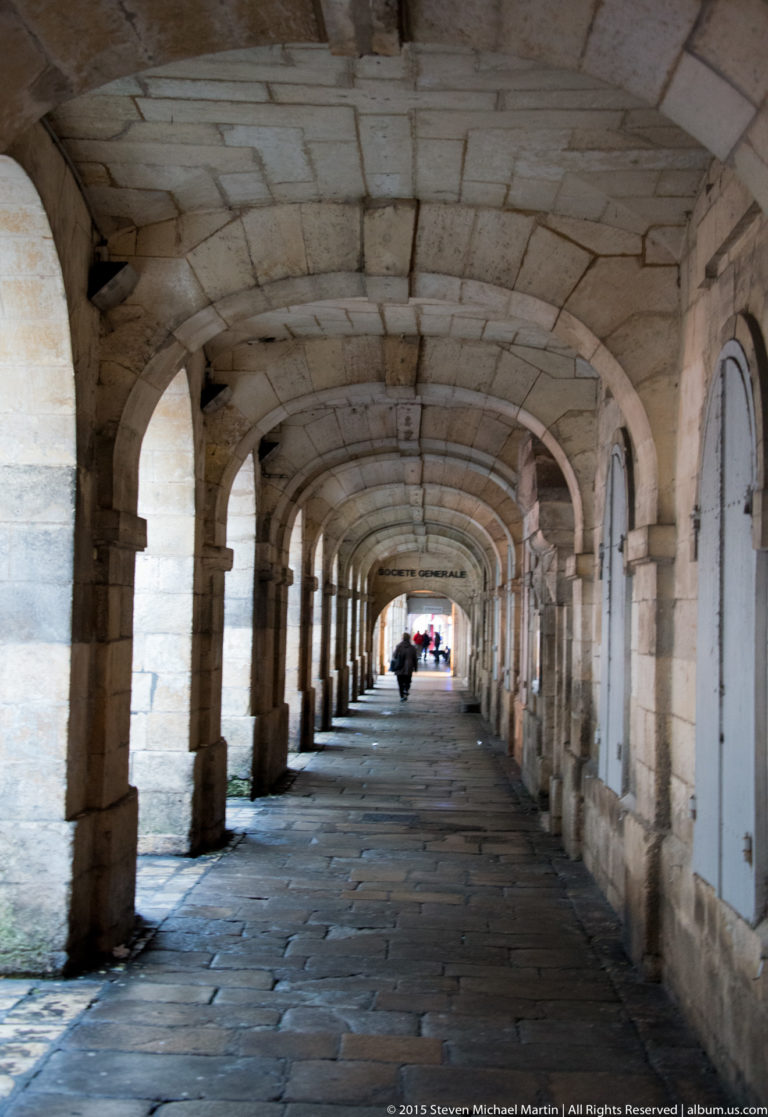 Long stone pedestrian arcade with repeated rounded arches and vaulted bays receding toward a bright opening.