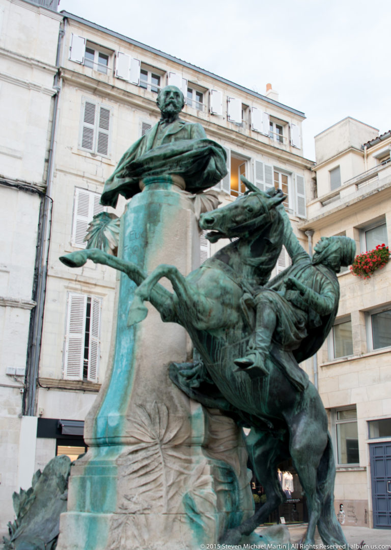Green-patinated bronze Eugène Fromentin monument with portrait figure, horse, and rider group on a stone pedestal in La Rochelle.