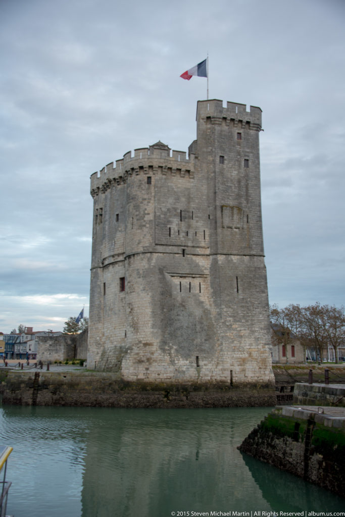 Massive crenellated stone Tour Saint-Nicolas beside the water at La Rochelle’s old harbor, with a French flag above.