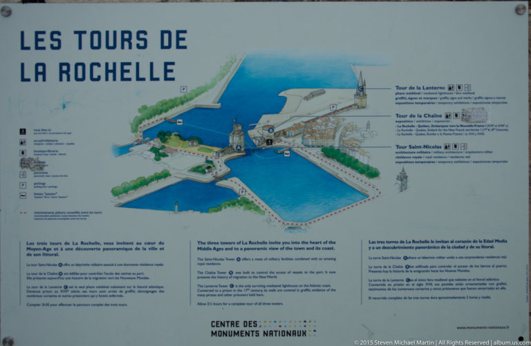 Outdoor interpretation sign with illustrated map of La Rochelle’s harbor towers and multilingual explanatory text.