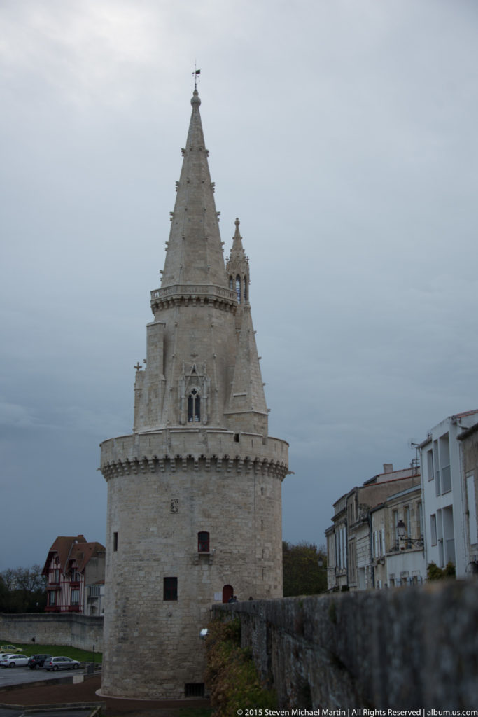 Tour de la Lanterne with tall conical stone spire, crenellated crown, Gothic openings, and adjoining historic wall in La Rochelle.