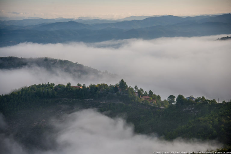 White cloud fills mountain valleys below dark wooded ridges, with layered hills fading into the distance.