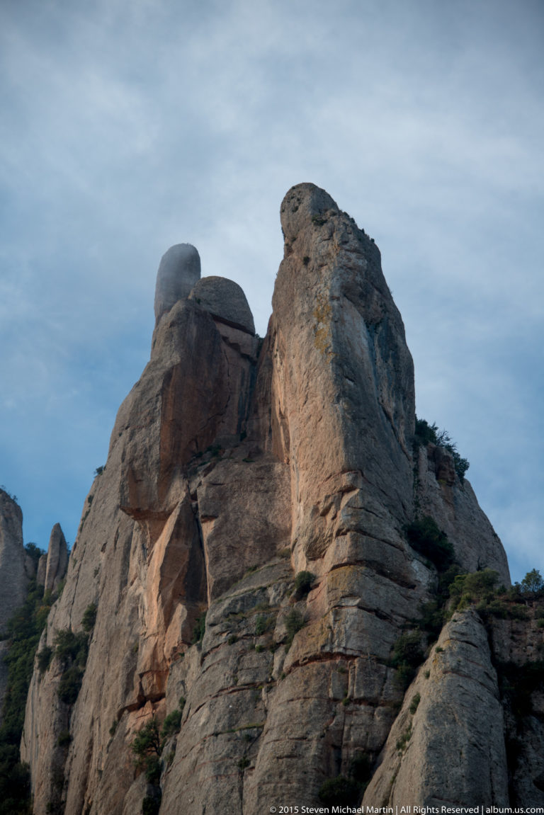 Rounded brown-gray rock crags of Montserrat rise steeply beneath a pale blue sky.