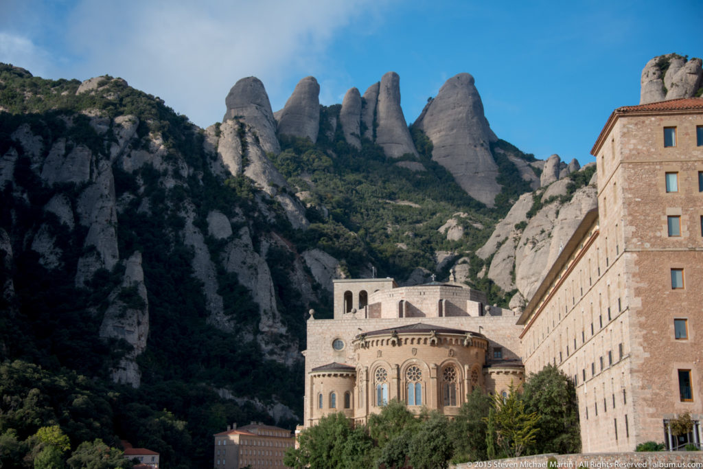 Santa Maria de Montserrat monastery buildings sit below towering jagged rock pinnacles on the mountainside.
