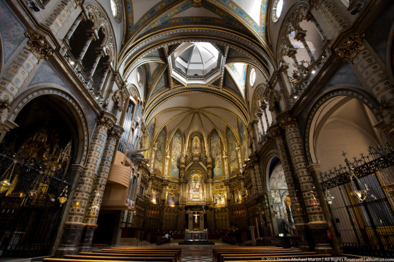 Decorated sanctuary of Montserrat basilica beneath ribbed vaulting, with gilded altar and iron screens.