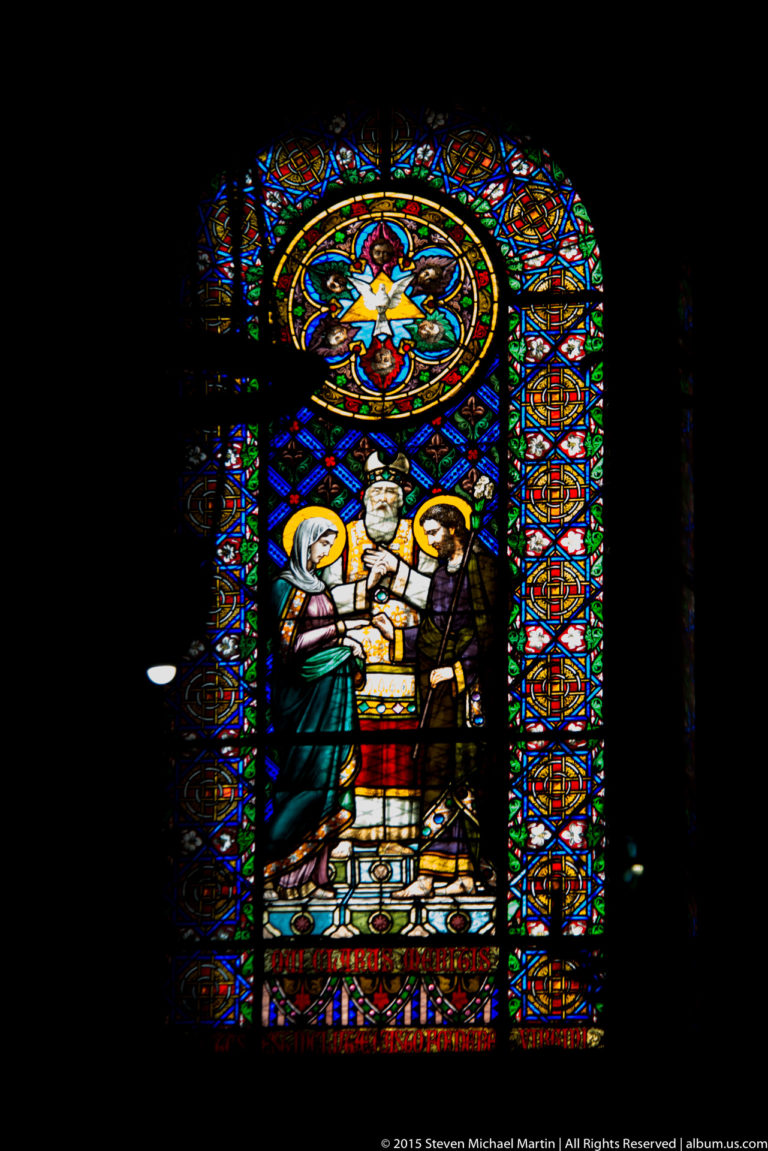 Bright figurative stained-glass window with haloed figures and vivid red, blue, green, and gold glass.