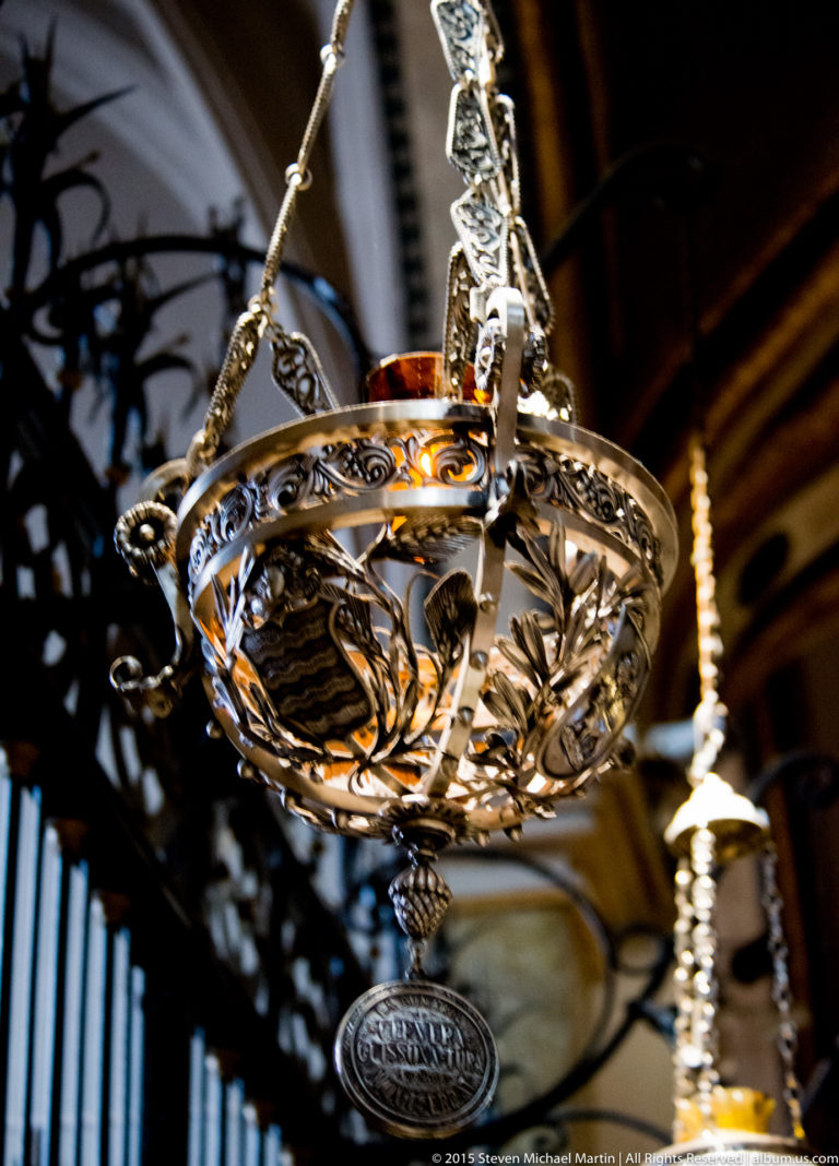 Pierced silver-colored hanging lamp suspended on decorative chains inside the Montserrat basilica.