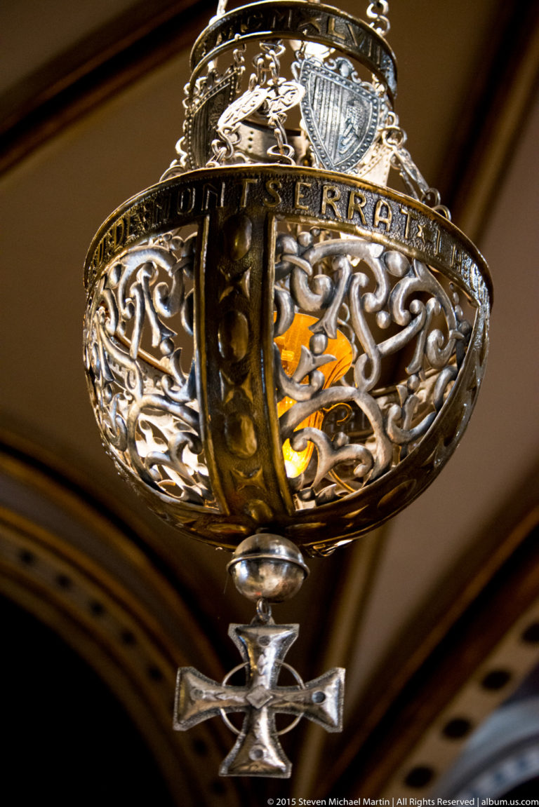 Close-up of ornate pierced hanging lamp with inscription band, glowing interior, and small pendant below.